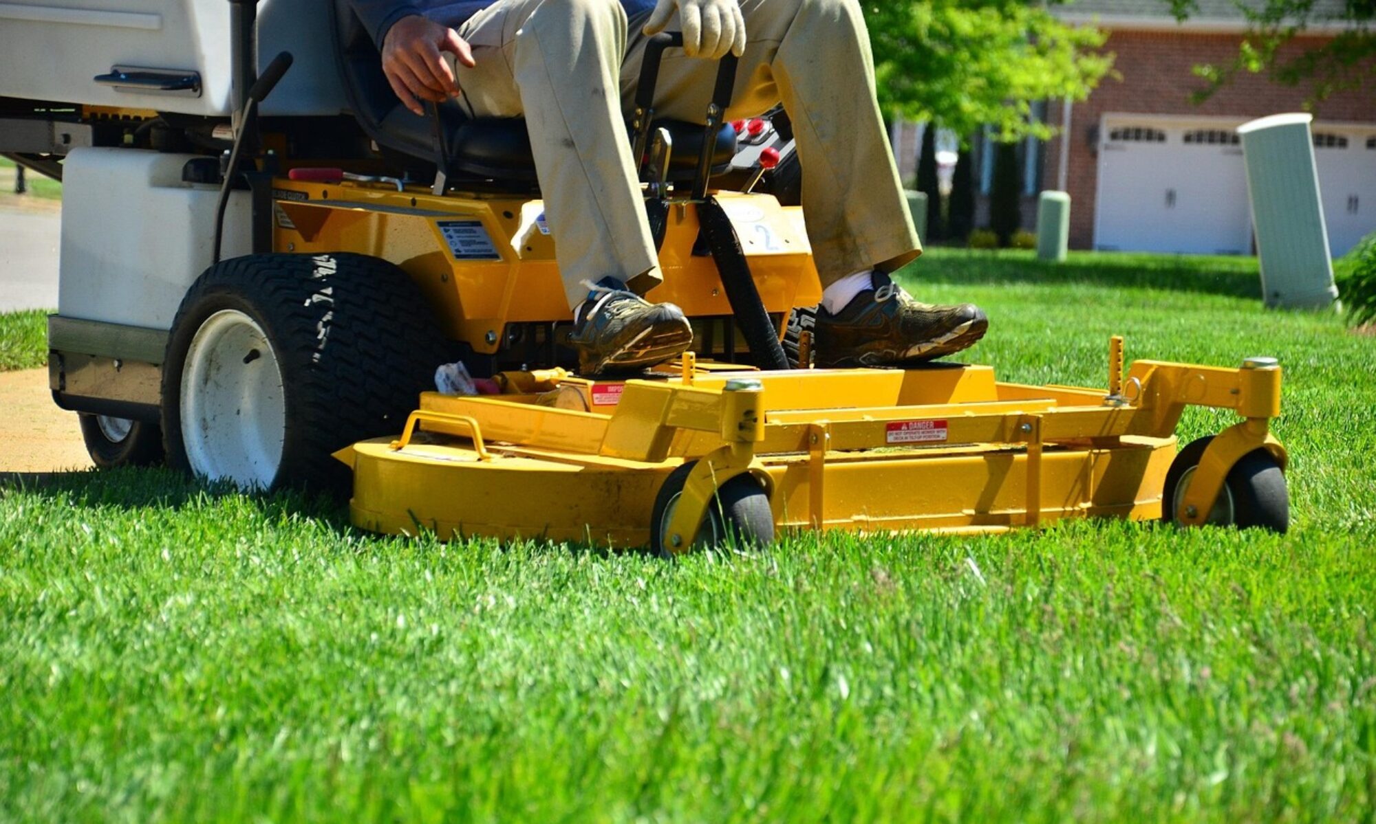Lawn care professional mowing a green backyard with a push mower in summer sunlight